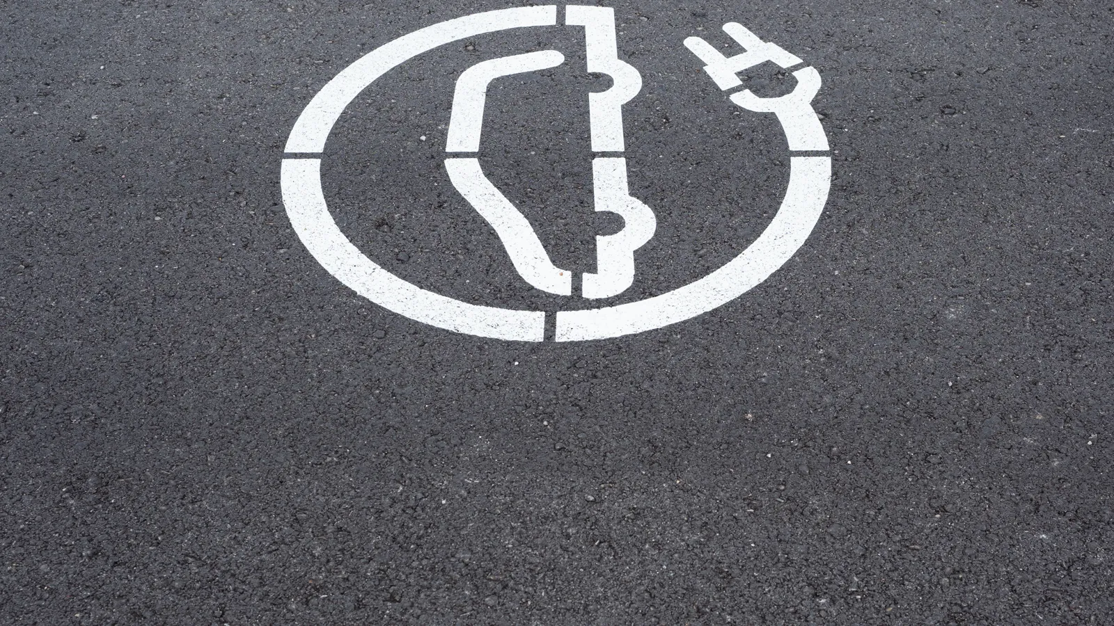 White electric vehicle charging symbol painted on asphalt next to a yellow line